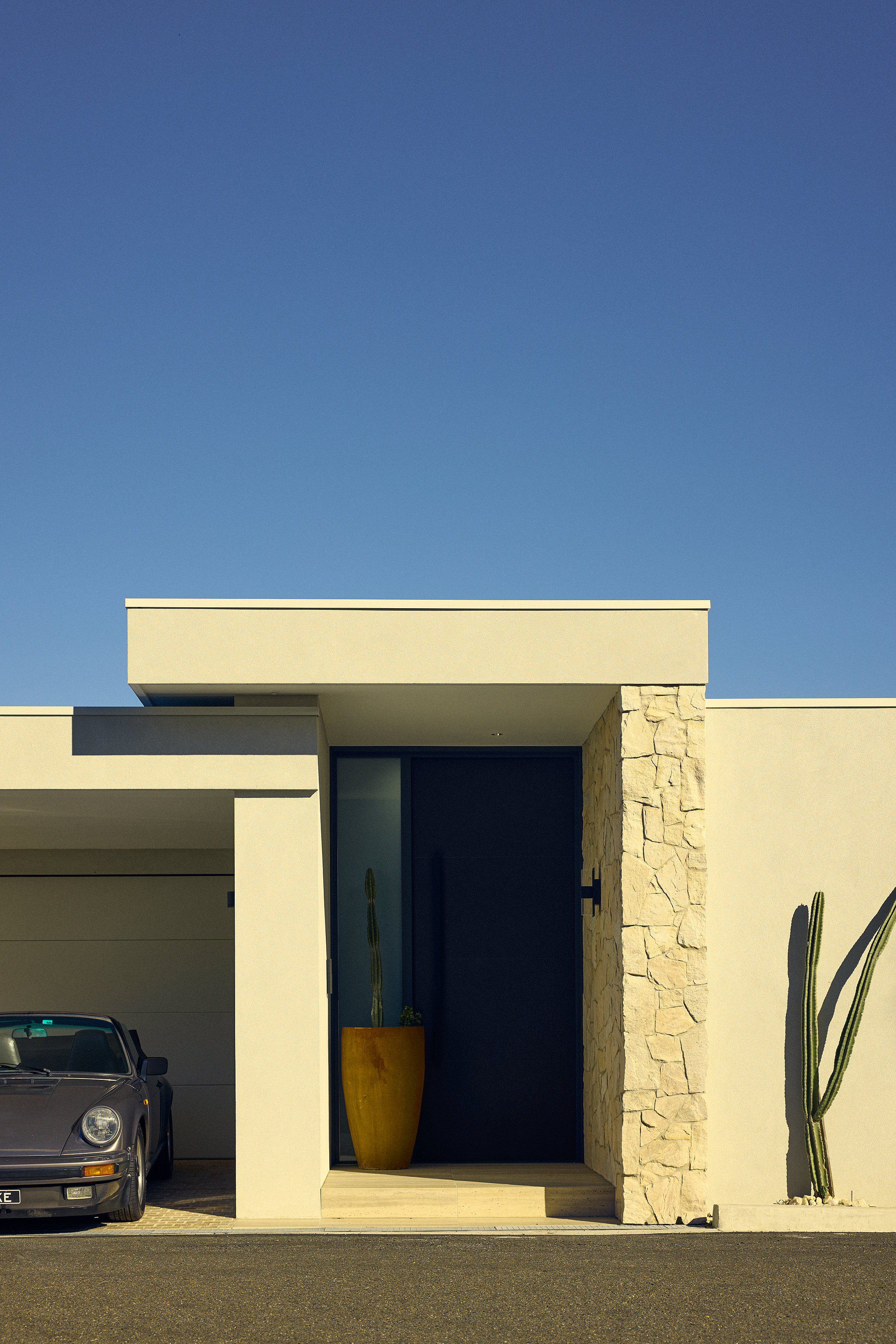 Palme Hus, entry and garage, stone pier and cactus against a deep blue sky